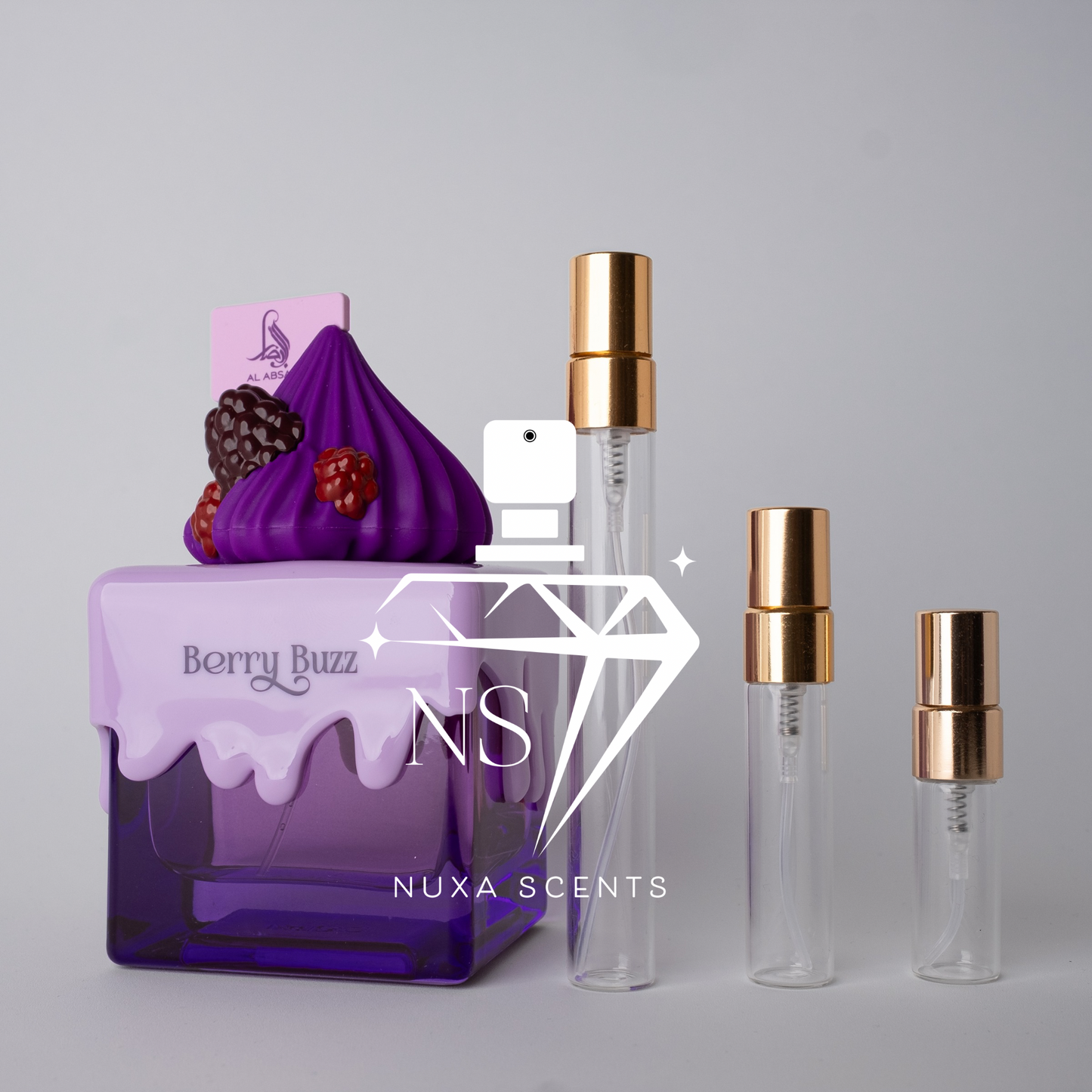Purple perfume bottle with 'Berry Buzz' flavor and two clear bottles with gold caps on a gray background, featuring Nuxa Scents branding.