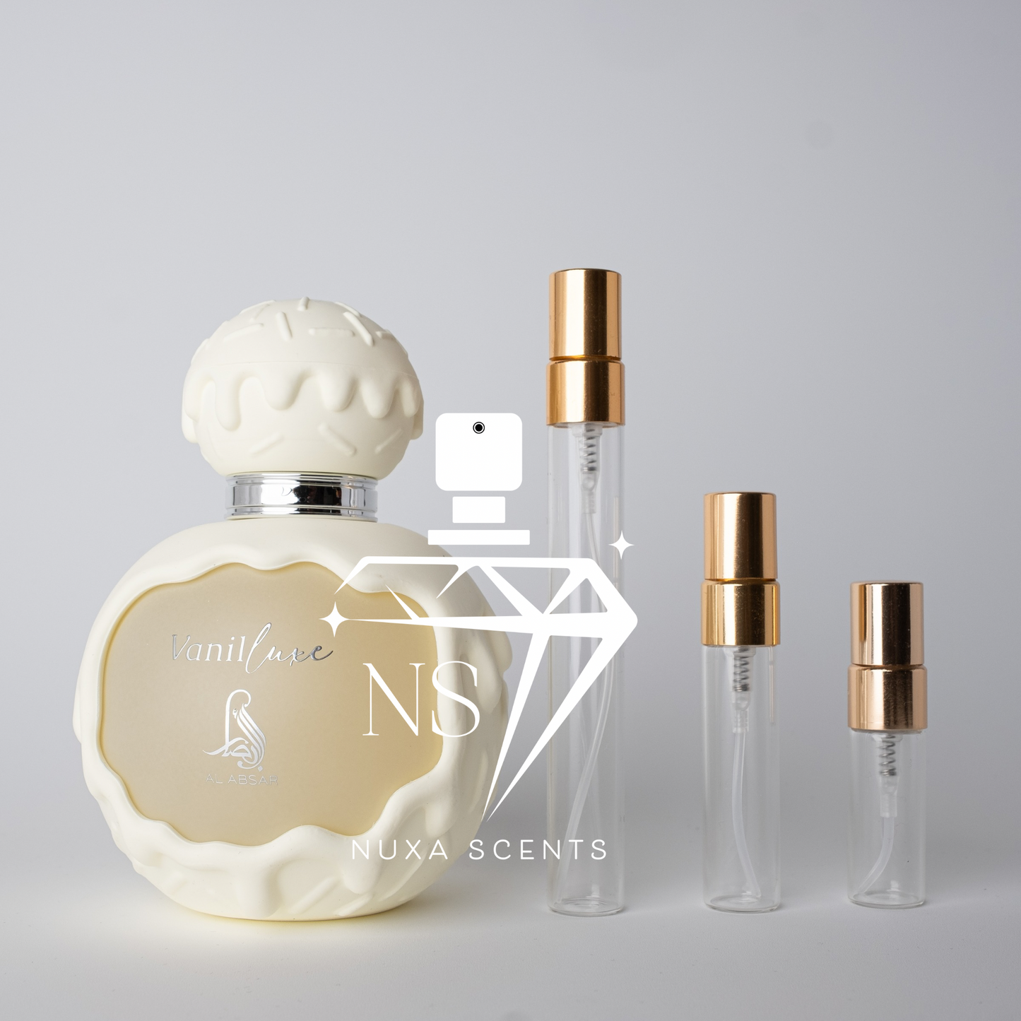 Perfume bottle with gold cap and smaller bottles on a gray background, featuring Nuxa Scents branding.