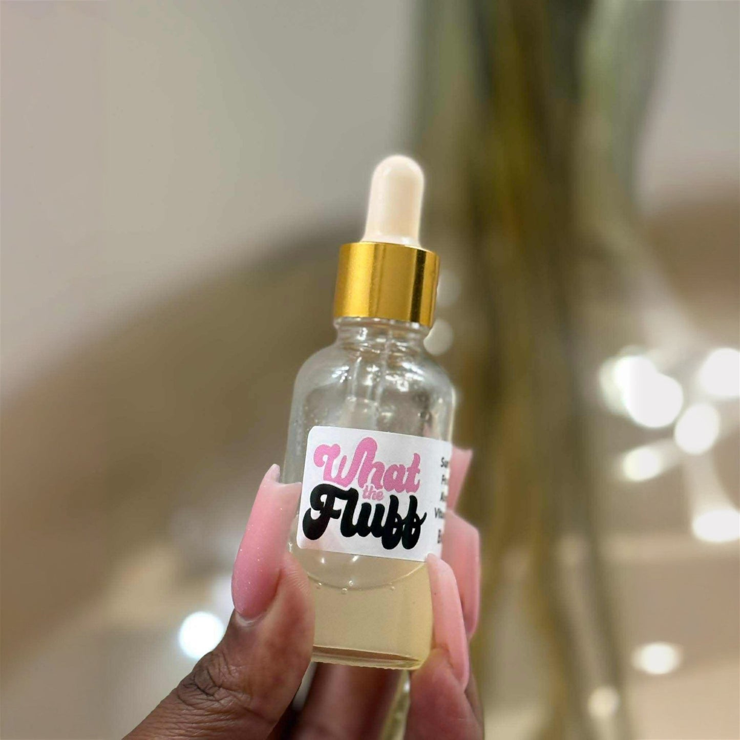 Bottle of 'What Fluff' with a dropper held by a hand against a blurred background
