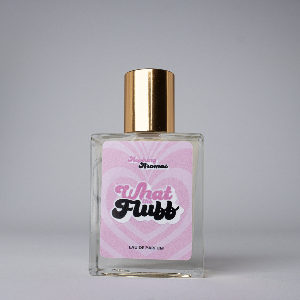 Perfume bottle with gold cap and pink label on a gray background with aspiring aromas what the fluff branding
