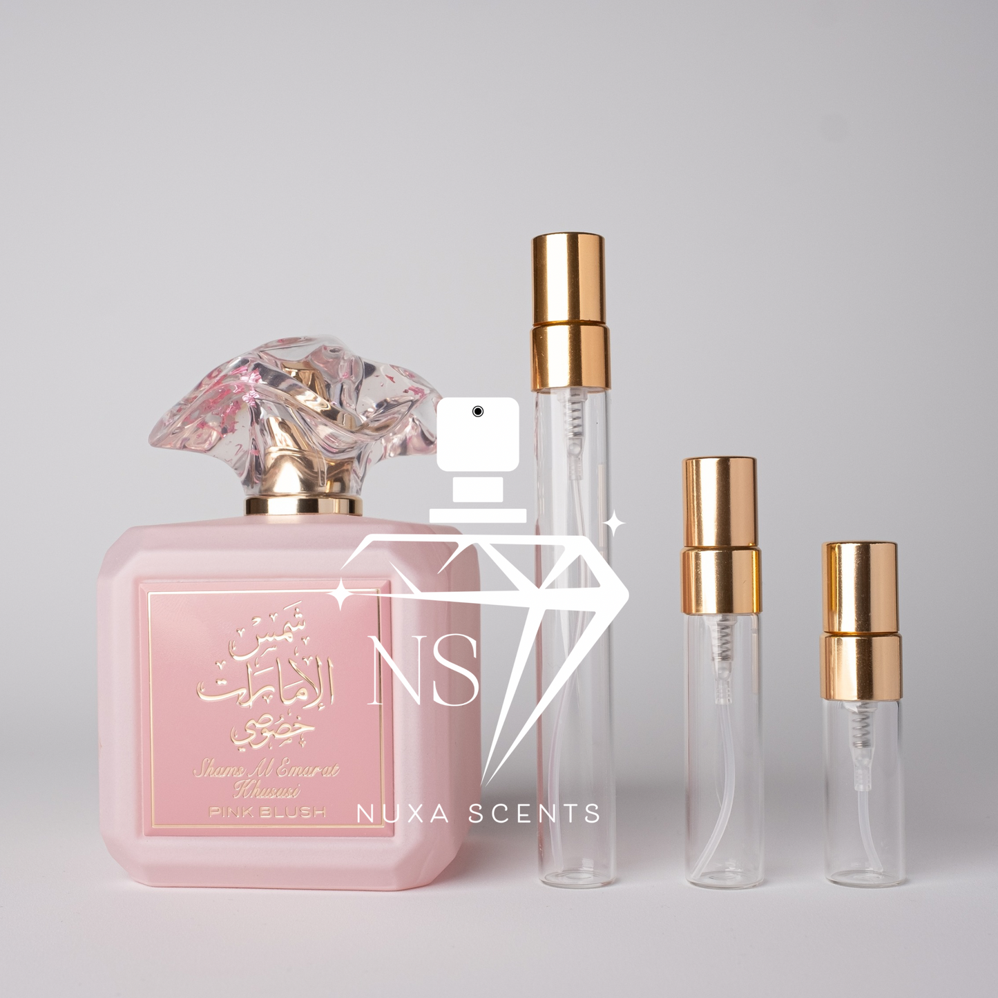 Pink perfume bottle with gold cap and clear bottles with gold caps on a light gray background, featuring Nuxa Scents logo.