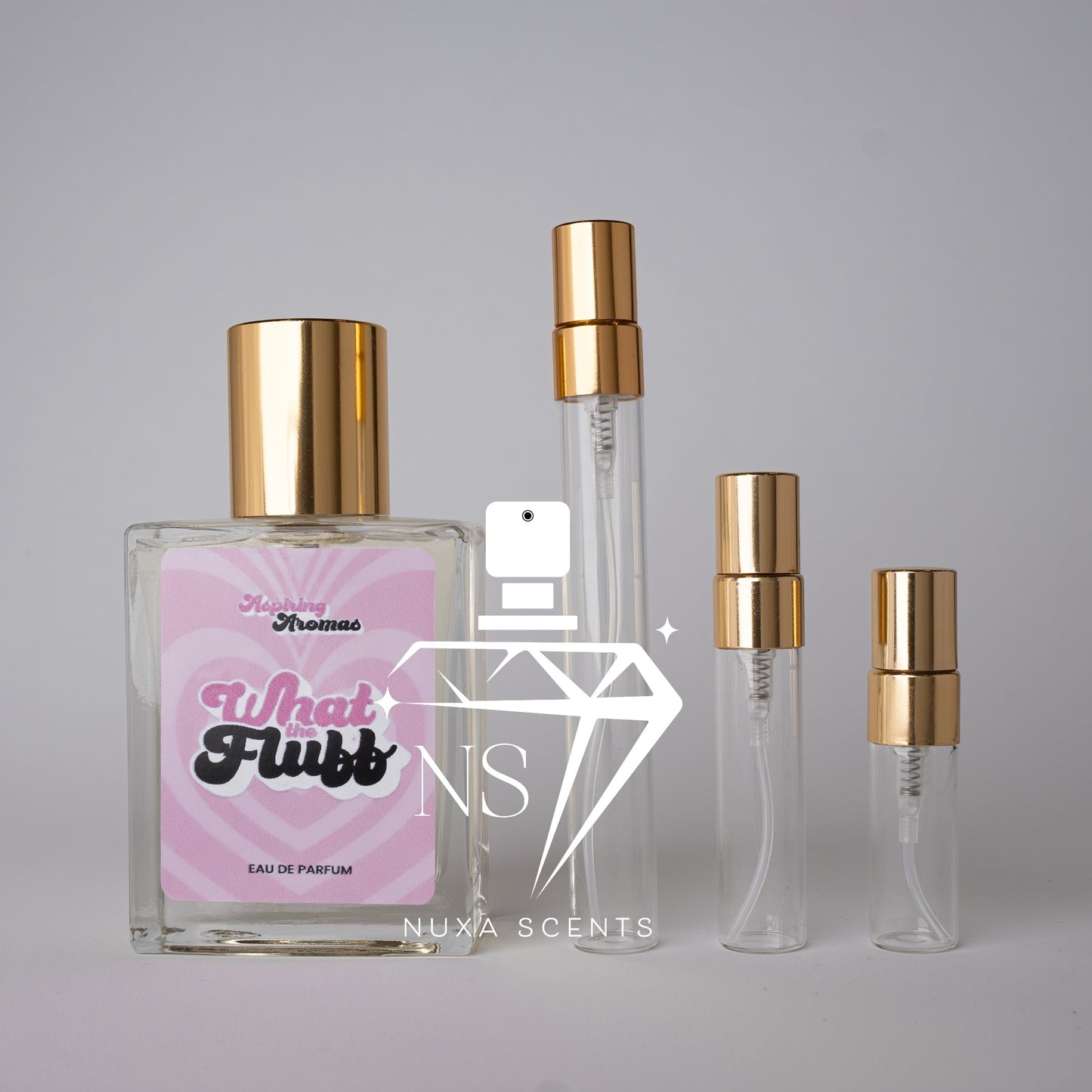 Set of perfume bottles with gold caps on a gray background, featuring what the Fluff aspiring aromas branding.
