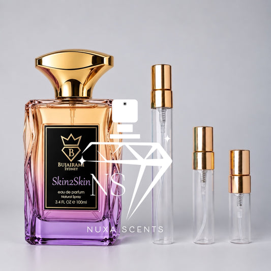 Bujairami Sydney Skin2Skin 100ml Eau de Parfum bottle featuring peach-to-lilac gradient glass, a sculpted gold cap and black-and-gold label, displayed beside three clear perfume sample decant spray bottles with gold atomisers on a clean light-grey studio background.