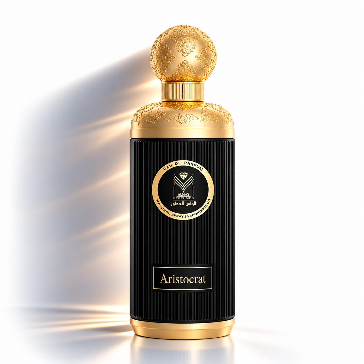 A luxury perfume bottle with a ribbed black body, gold cap and base, and a central circular gold-and-black label reading 'Aristocrat' and 'Eau de Parfum'. The bottle is photographed on a clean white background with dramatic side lighting and a soft reflection below.
