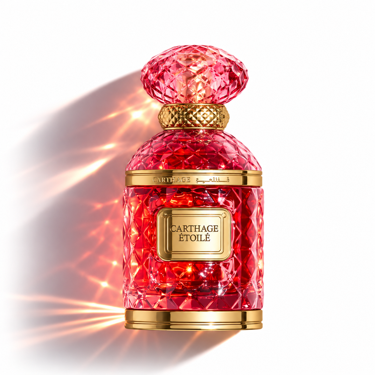 A luxury perfume bottle by Cartage Étoilé, featuring a faceted red crystal-like body and a gold-toned cap and label, set against a white background with dramatic light flares.