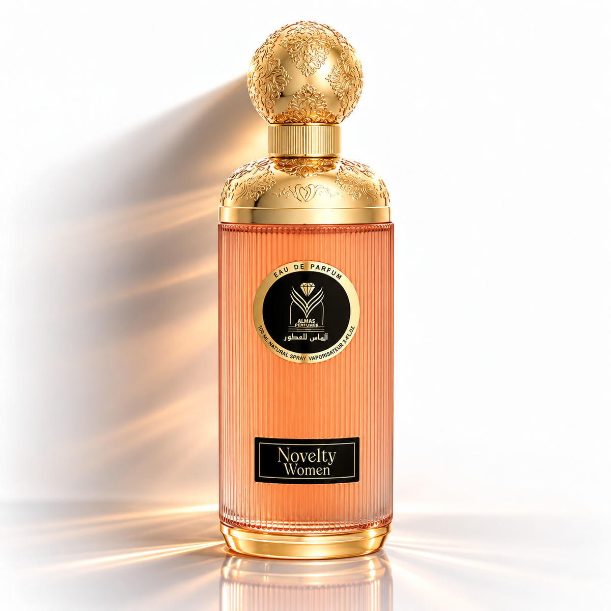 A luxury perfume bottle with a ribbed peach-pink glass body, ornate gold cap and collar, and a black circular label reading 'Eau de Parfum' and 'Novelty Women'. The bottle is centered on a clean white background with dramatic golden light rays shining from the left.